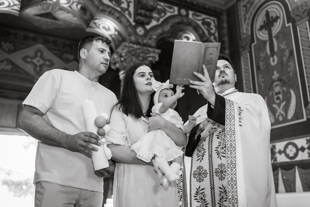 Nasii cu bebelusul in brate, citind Crezul in biserica. Fotograf Botez Bucuresti.