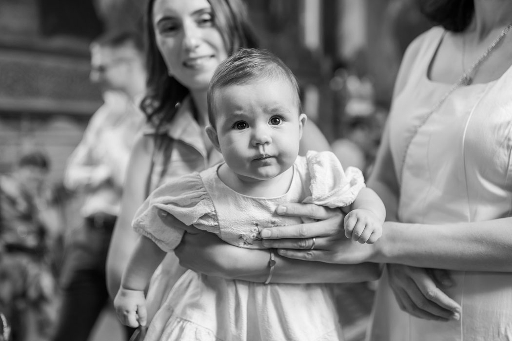 Bebelusul in biserica, dupa botez, surprins de fotograf in bratele nasei si al mamei