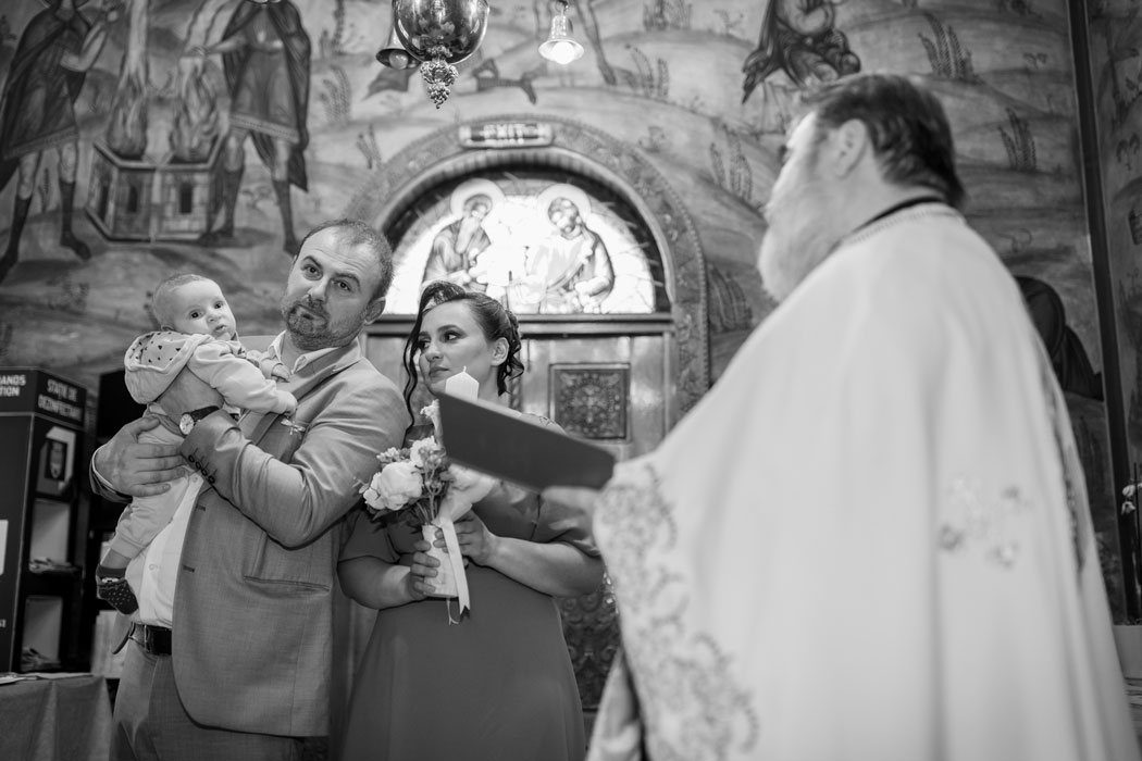 Expresia nasilor cu bebelusul in brate cand citeste preotul, moment surprins de fotograf botez Bucuresti.